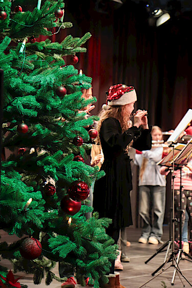 Im Vordergrund ein Weihnachtsbaum, im Hintergrund das Flötenensemble auf der Bühne